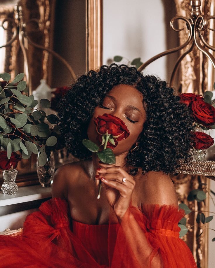 a black woman wearing a red dress and smelling a red rose
