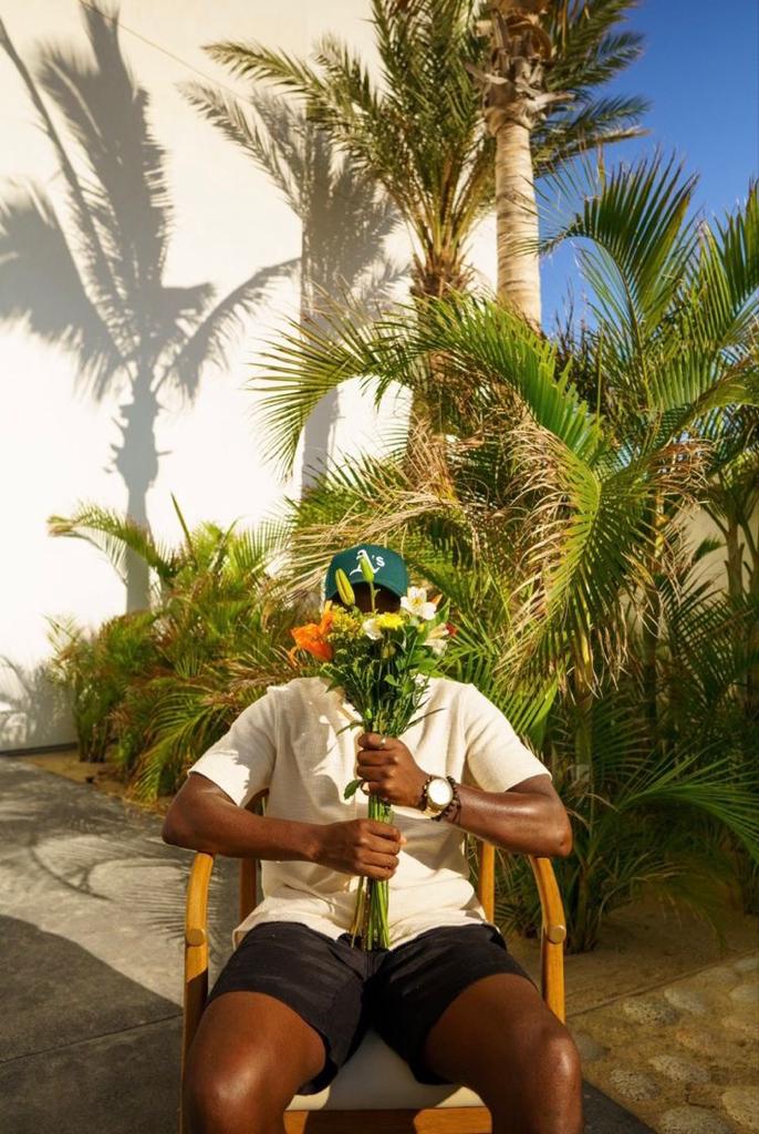A MAN HOLDING FLOWERS TO COVER HIS FACE AND SITTING ON A CHAIR
